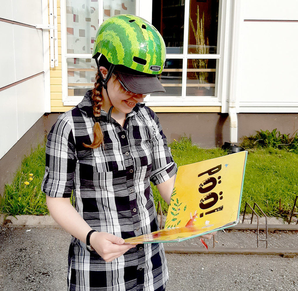 Ihminen lukee melonin näköinen kypärä päässä kirjaa ulkona