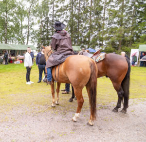 Lännenratsastusta Yli-Kannuksen Wanhanajanmarkkinoilla 2022. Kuvassa kaksi hevosta, ratsastaja ja markkiniväkeä.
